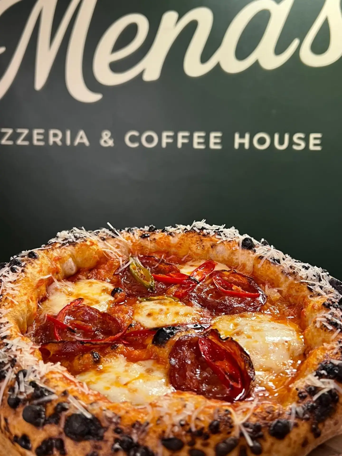 Mena’s wood-fired pizza in front of the restaurant’s green brand wall